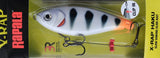 Rapala X-RAP Haku slow sinking glide bait in its original retail packaging, featuring a white and black tiger-stripe design with a bright orange tail, shown against a textured beige background.